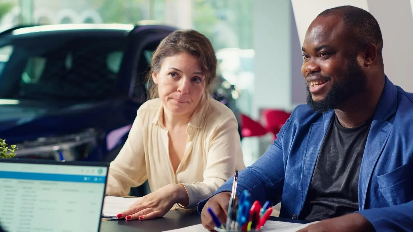 Customers in a showroom filling out a credit application to purchase a new car.